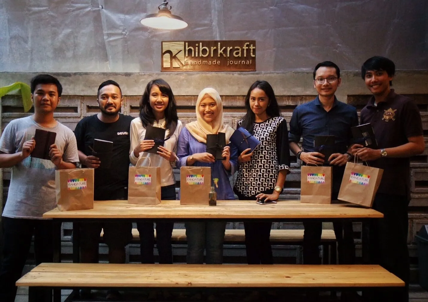 Delapan peserta Hibrkraft Experience berdiri di depan spanduk Hibrkraft, masing-masing memegang jurnal yang baru mereka buat
