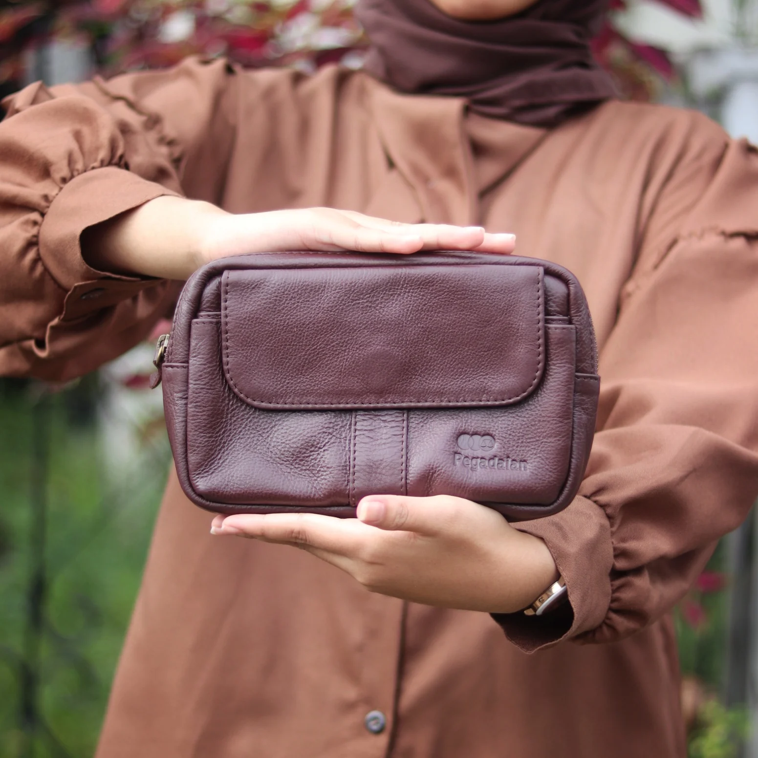 Perempuan berhijab memegang dompet kulit berlogo klien, hasil pengerjaan bengkel Hibrkraft.