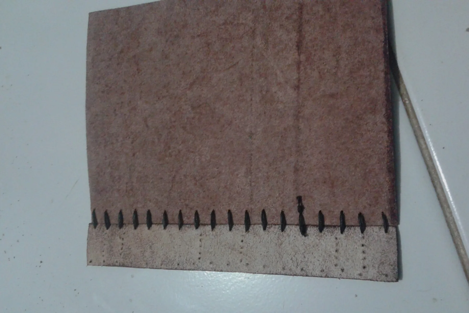 Detail jahitan tangan pada punggung sampul kulit, benang menembus lipatan kertas