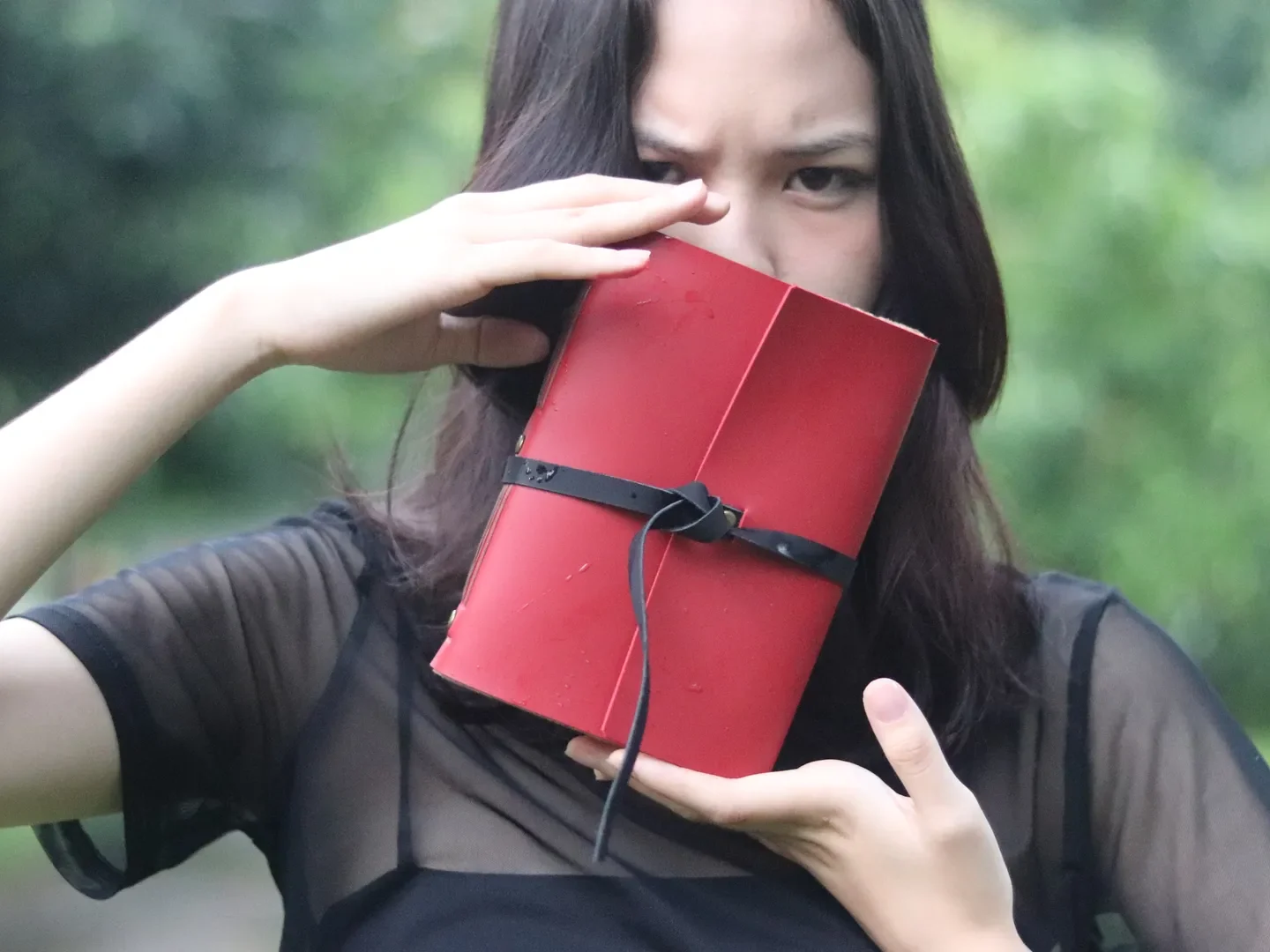 Perempuan memegang jurnal kulit merah di depan wajahnya