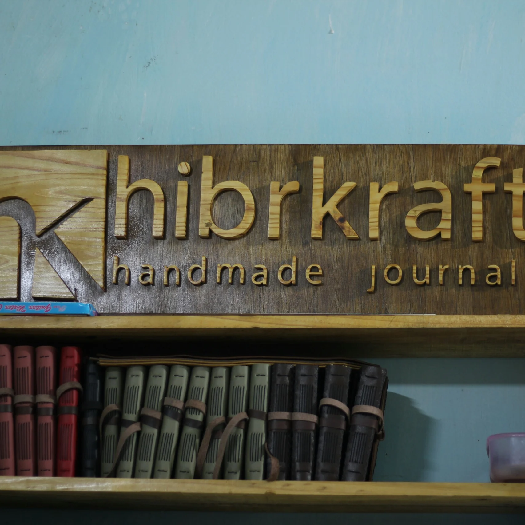 A wooden hibrkraft sign mounted above a shelf filled with a collection of leather journals.