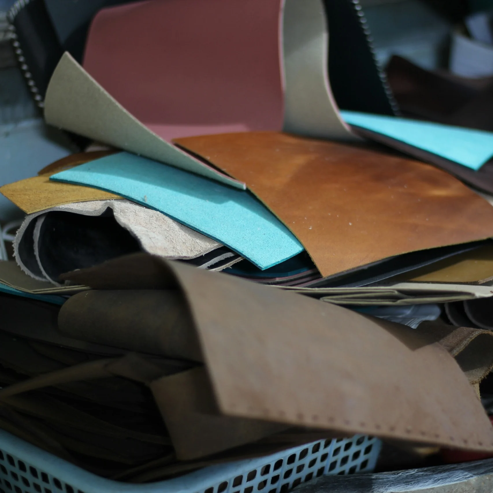 A pile of colorful leather scraps inside a plastic basket.