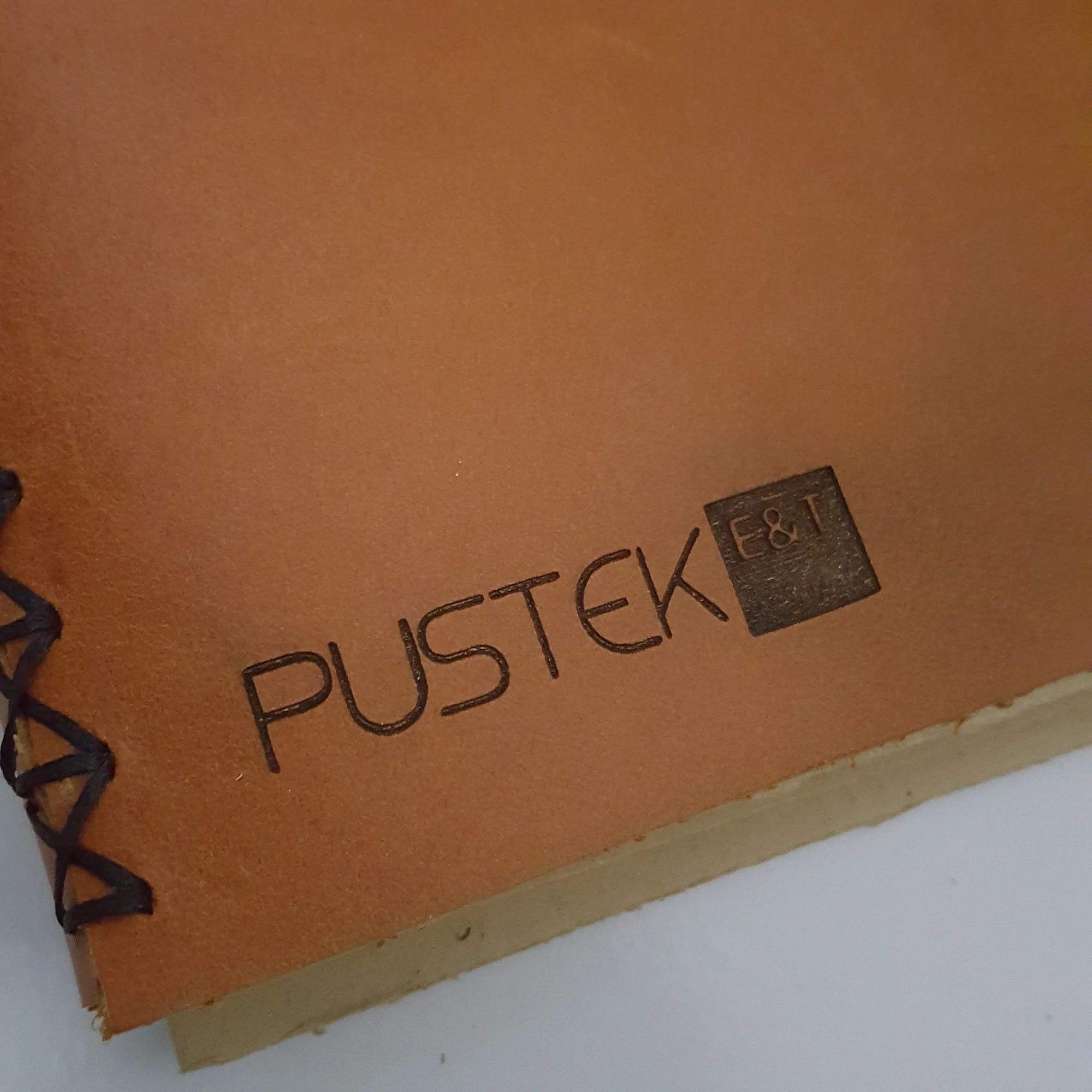 A brown leather journal cover featuring a debossed Pustek E&T logo.