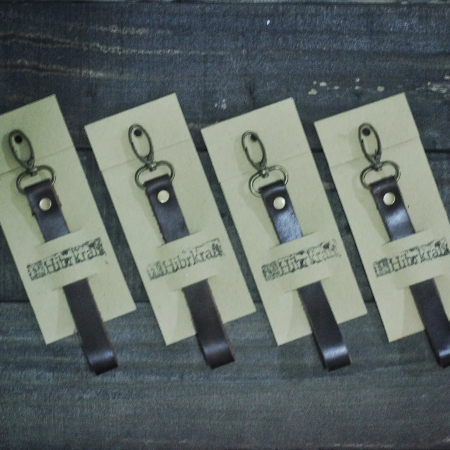 Four leather keychains with Hibrkraft logo on packaging cards.