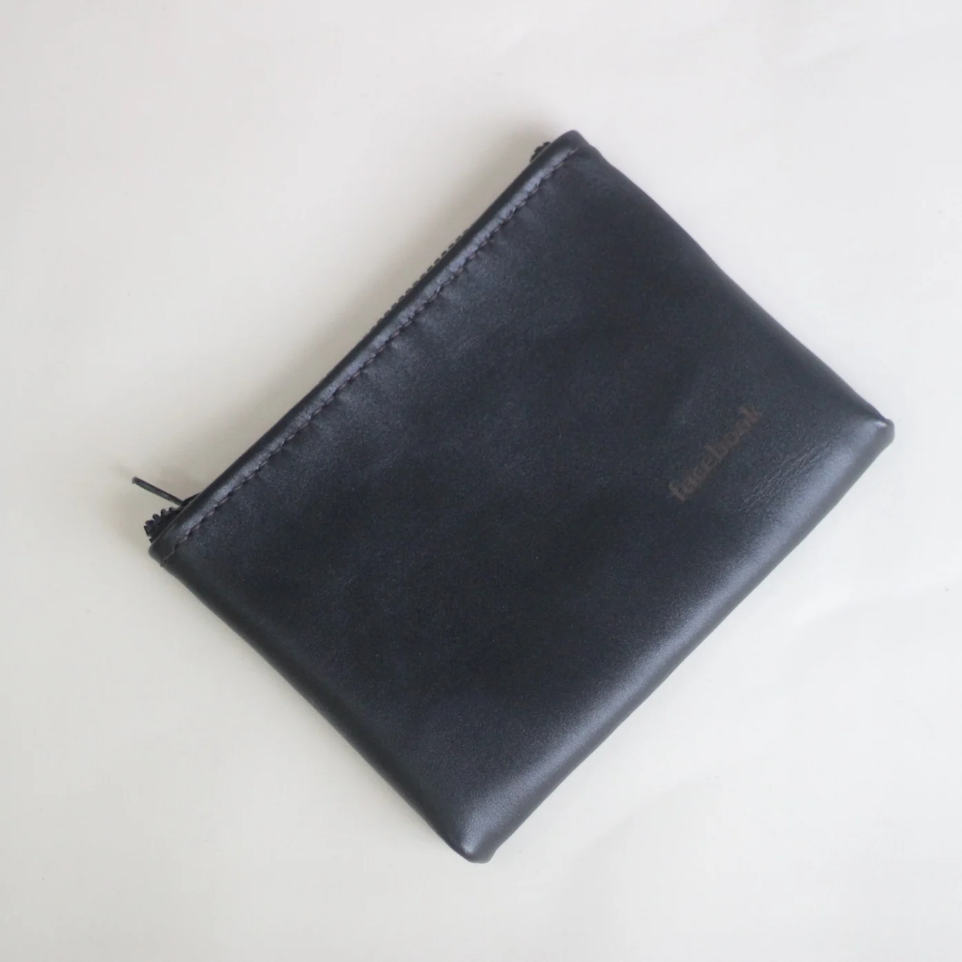A black leather zipper pouch with a debossed facebook logo.