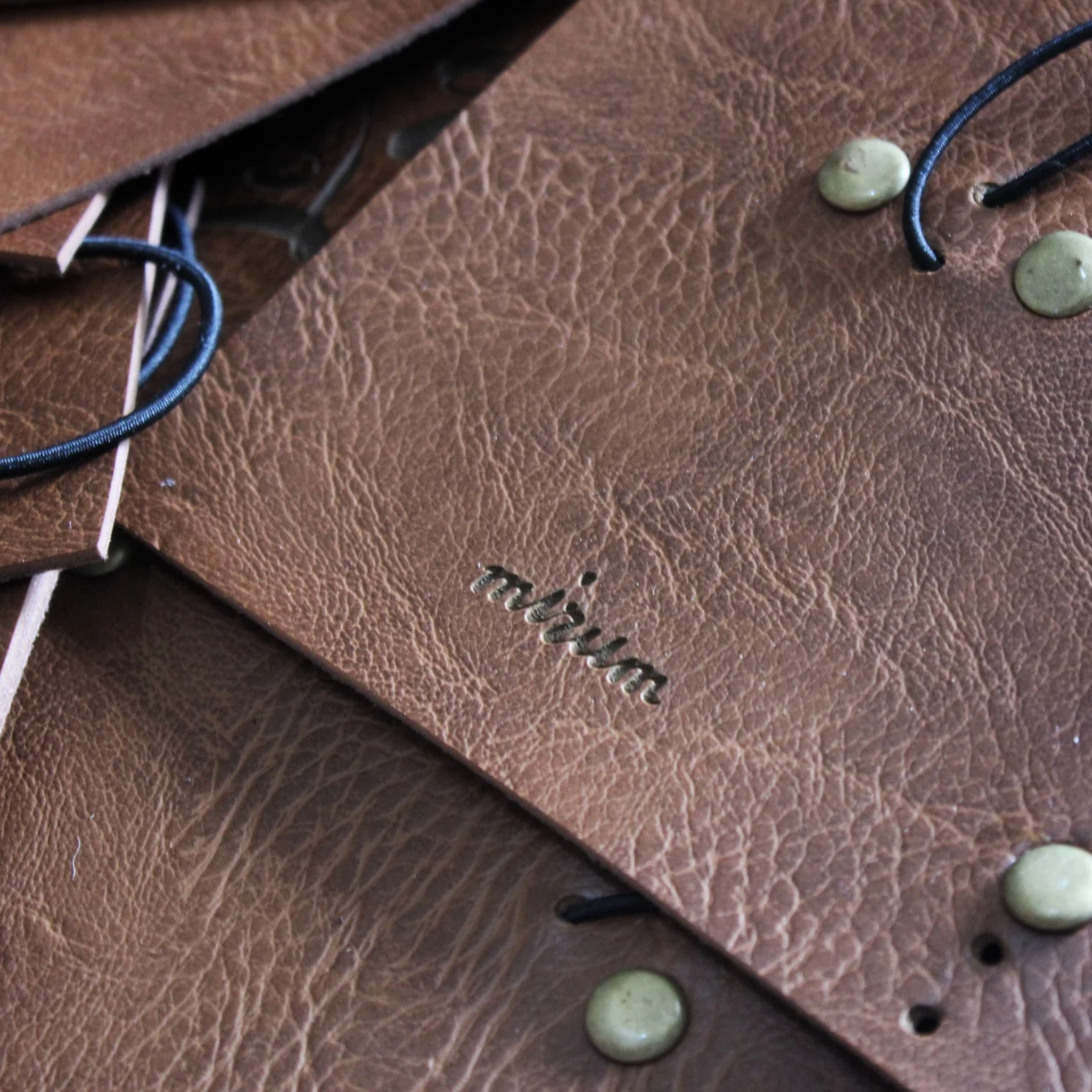 A stack of brown leather tags featuring debossed mirum text and metal rivets.