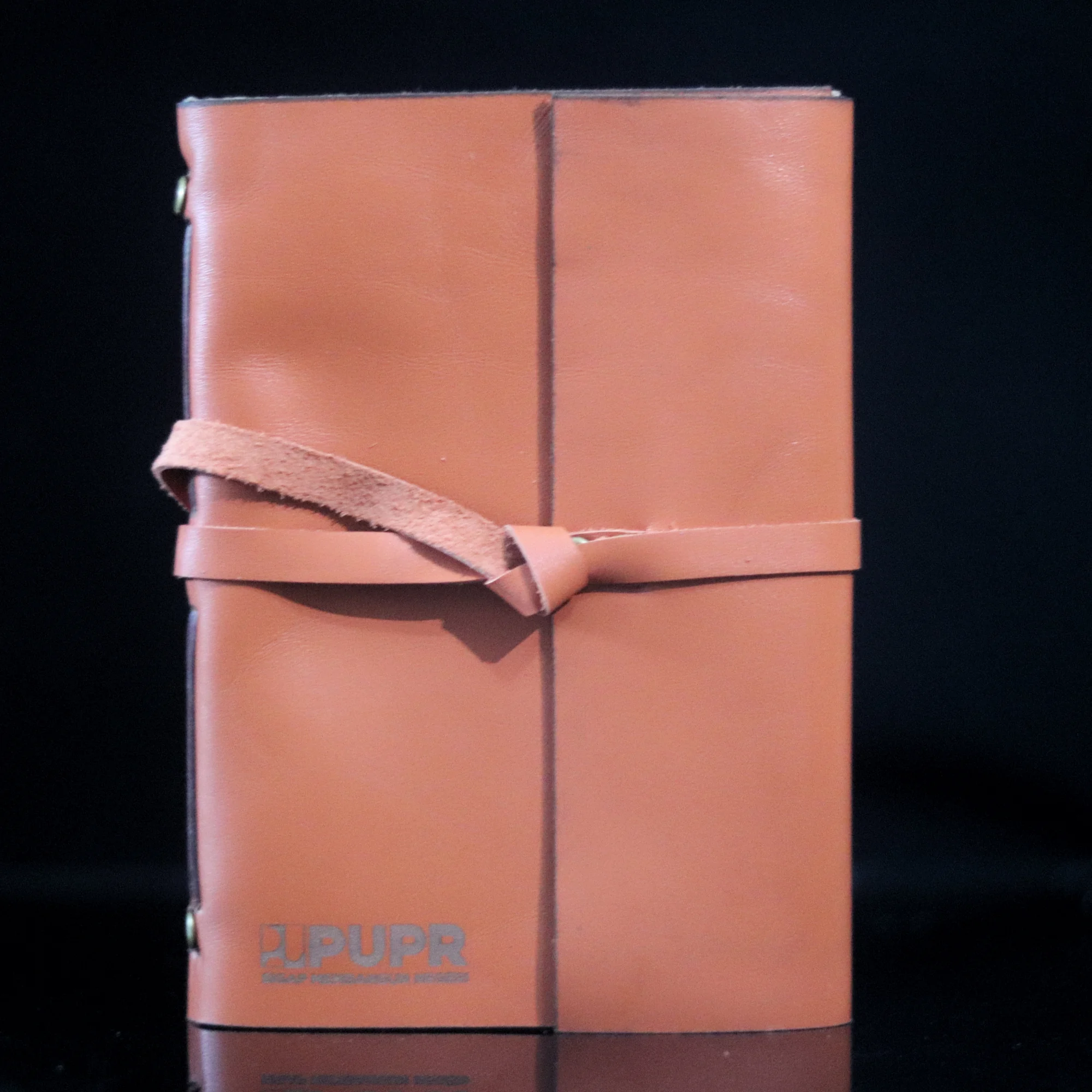A brown leather journal featuring the PUPR logo and a tie closure.