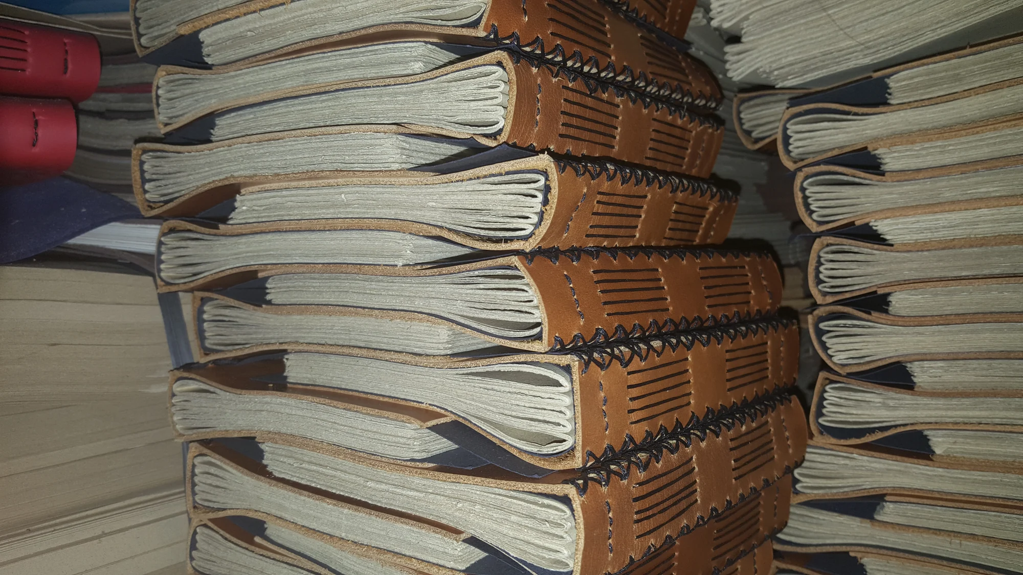 Tumpukan jurnal kulit PPLI dengan jahitan coptic yang terlihat