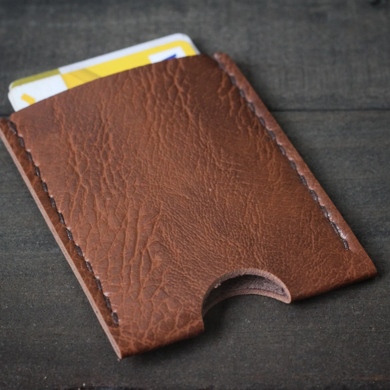 Brown leather card holder with hand stitching on a wooden surface.