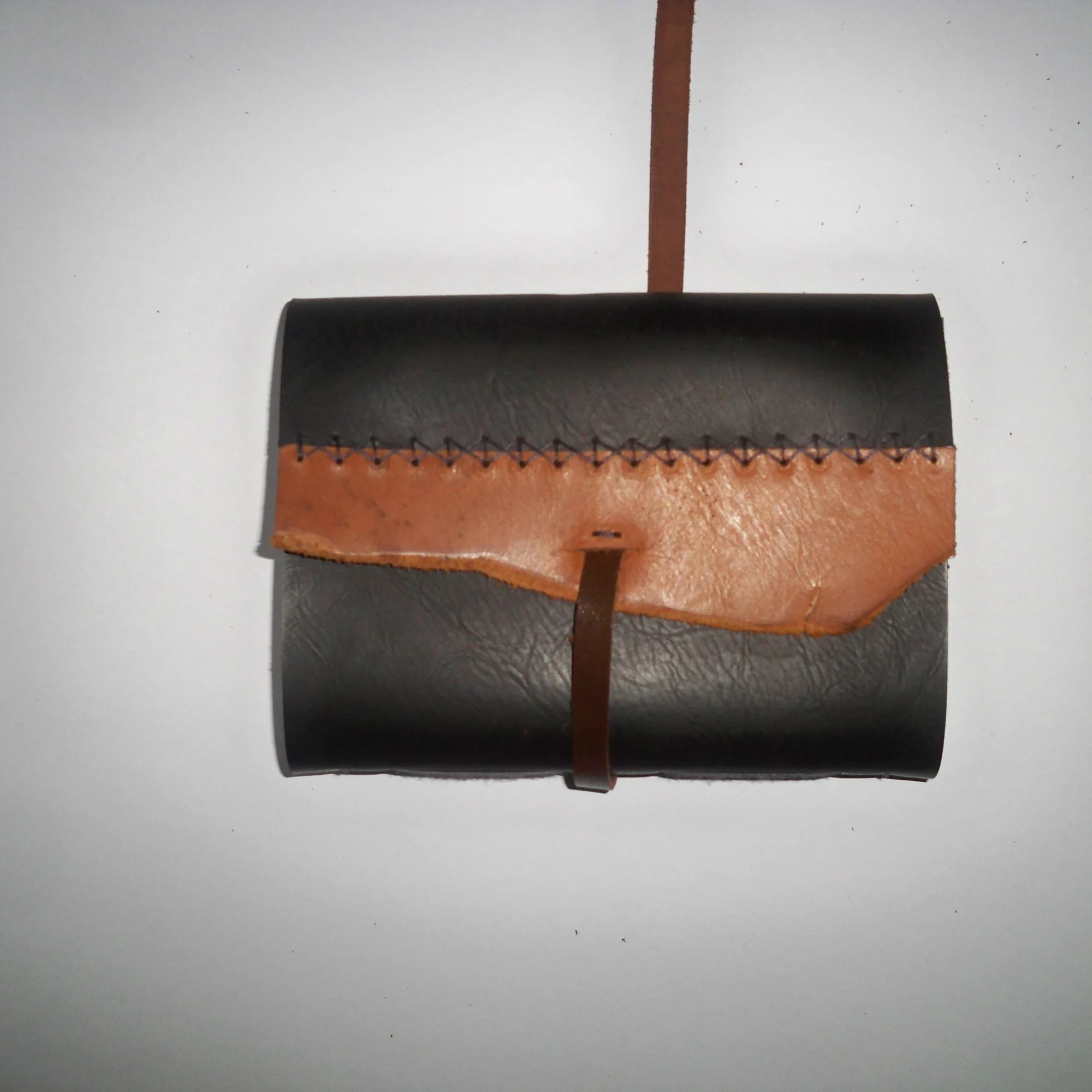 A penumbra leather journal with a strap closure hanging against a wall.