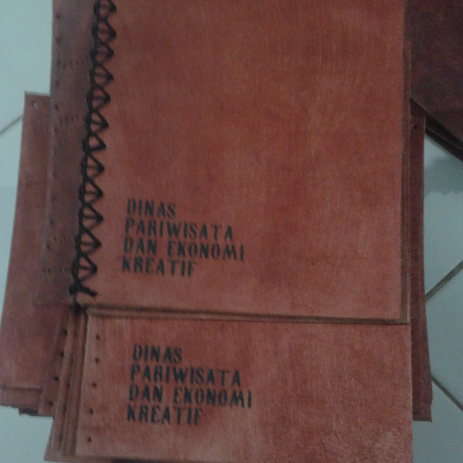 A stack of leather journal covers featuring the debossed logo of Dinas Pariwisata dan Ekonomi Kreati