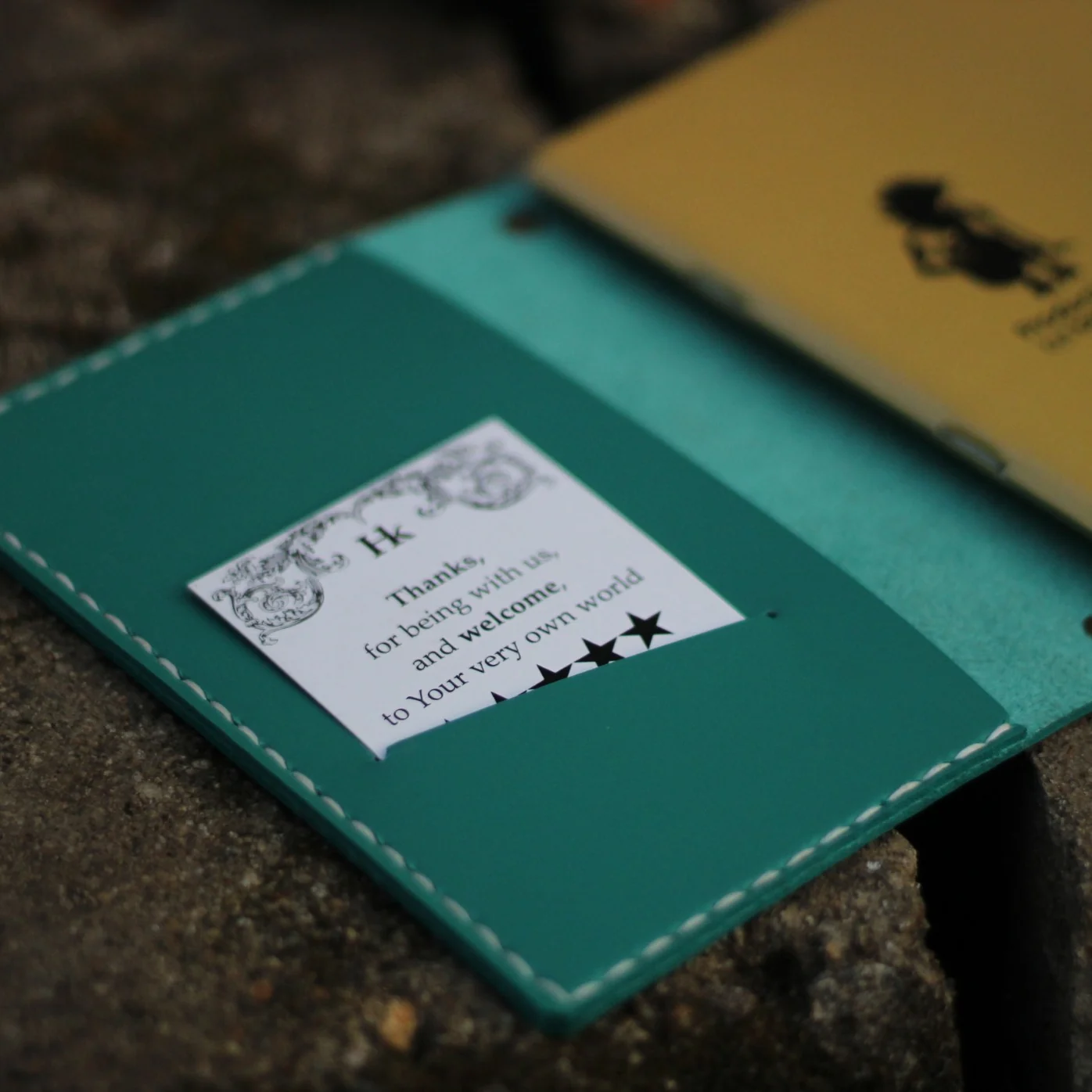 Sampul jurnal kulit teal dengan kartu ucapan terselip di kantongnya
