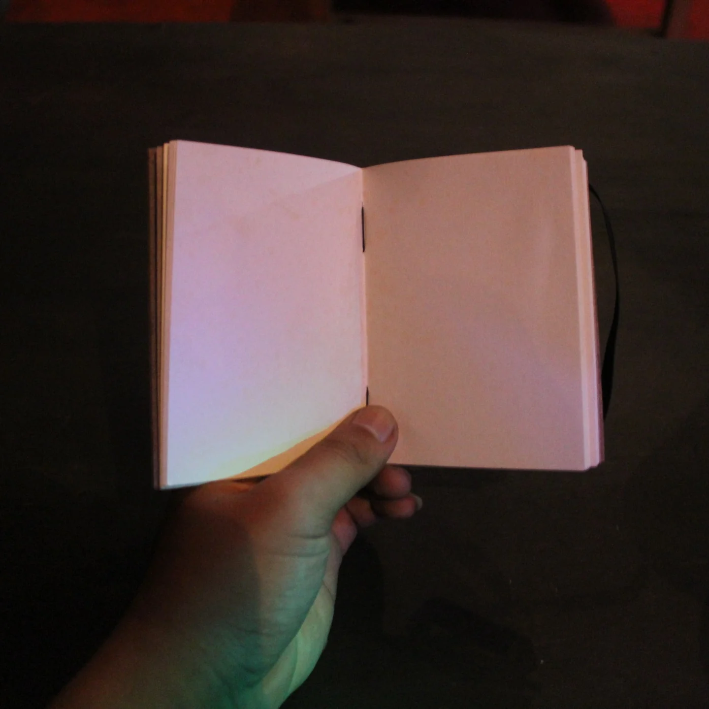 Tangan memegang buku catatan kecil yang terbuka dengan halaman kosong