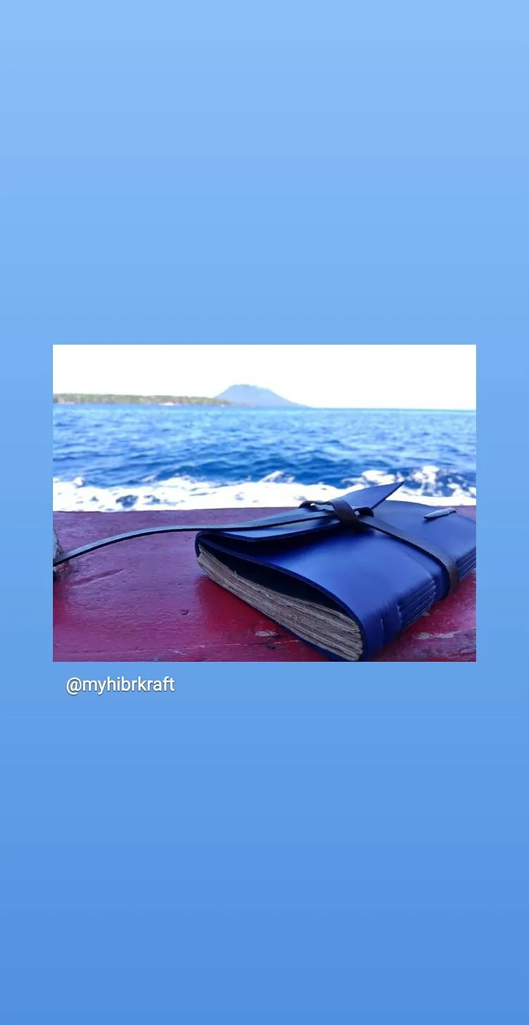 Story Instagram: jurnal kulit biru bertali lilit di atas geladak perahu merah, laut dan pulau di kejauhan