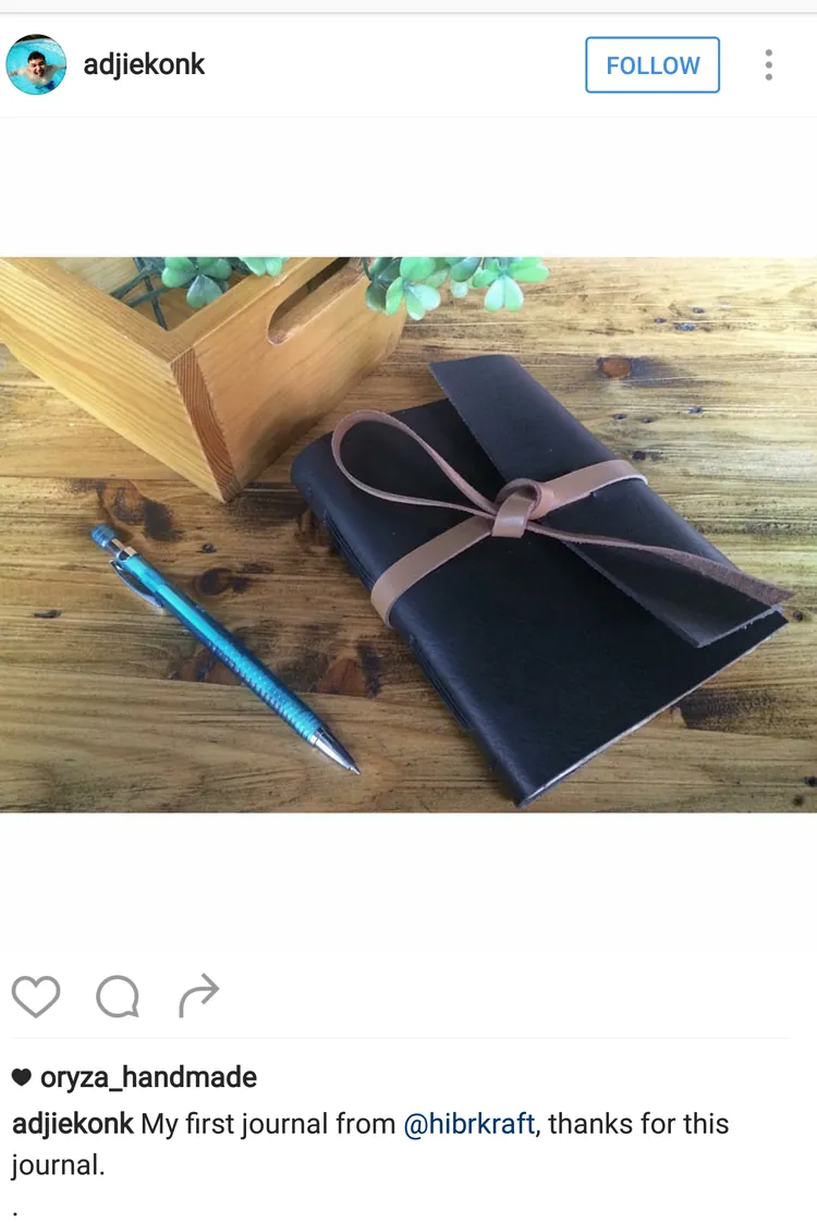 Unggahan Instagram @adjiekonk: jurnal kulit biru tua bertali tan di atas meja kayu dengan sebuah pena