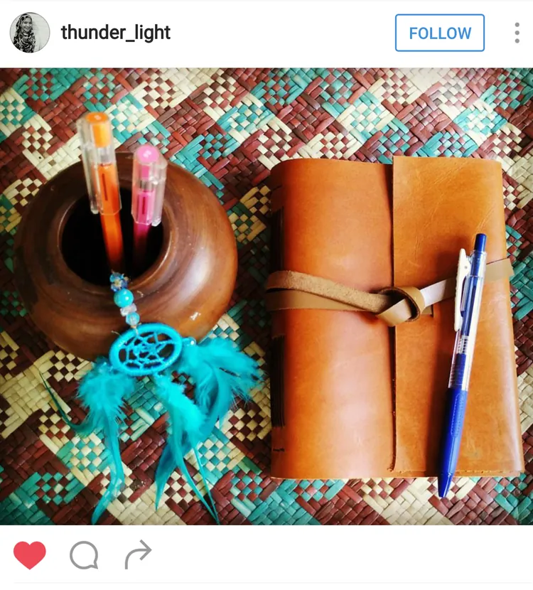 Unggahan Instagram @thunder_light: jurnal kulit tan bertali lilit di atas lantai bermotif, bersama pot pena dan penangkap mimpi biru