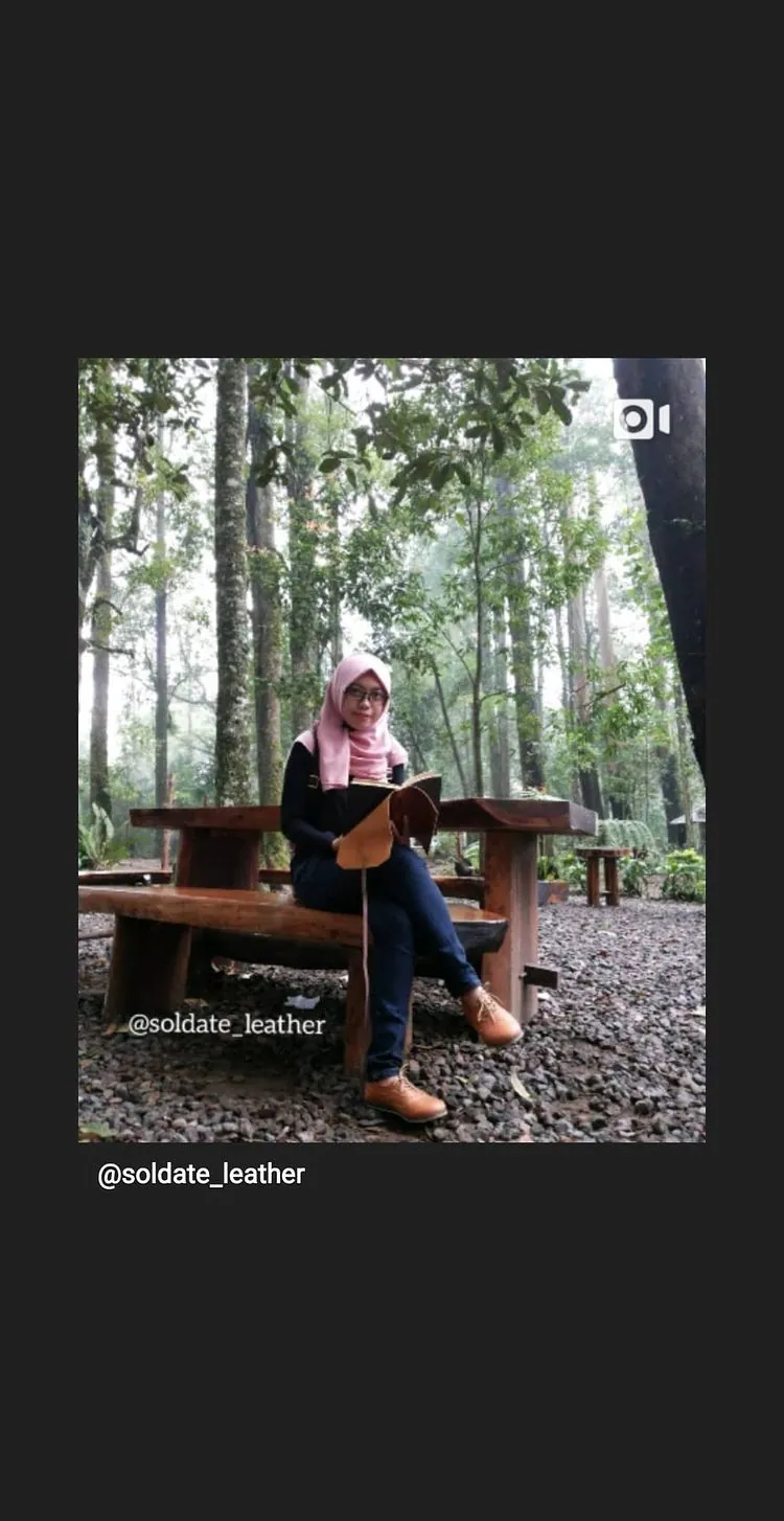 Story Instagram: perempuan berhijab menulis di jurnal sambil duduk di bangku kayu di tengah hutan