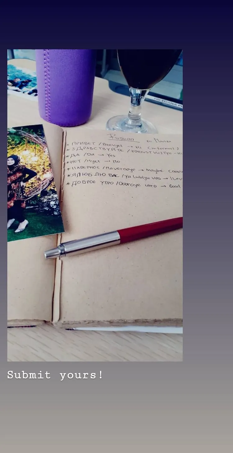 Story Instagram: jurnal terbuka berisi catatan tulisan tangan beraksara Kiril, dengan pena merah putih di atasnya