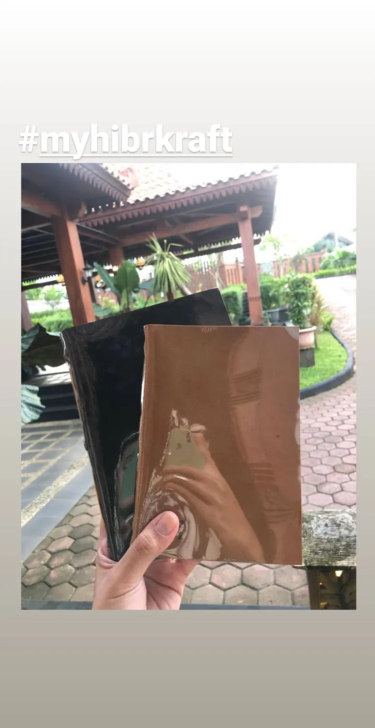 Story Instagram bertagar #myhibrkraft: dua jurnal, gelap dan tan, dipegang di atas jalan setapak berpaving heksagonal