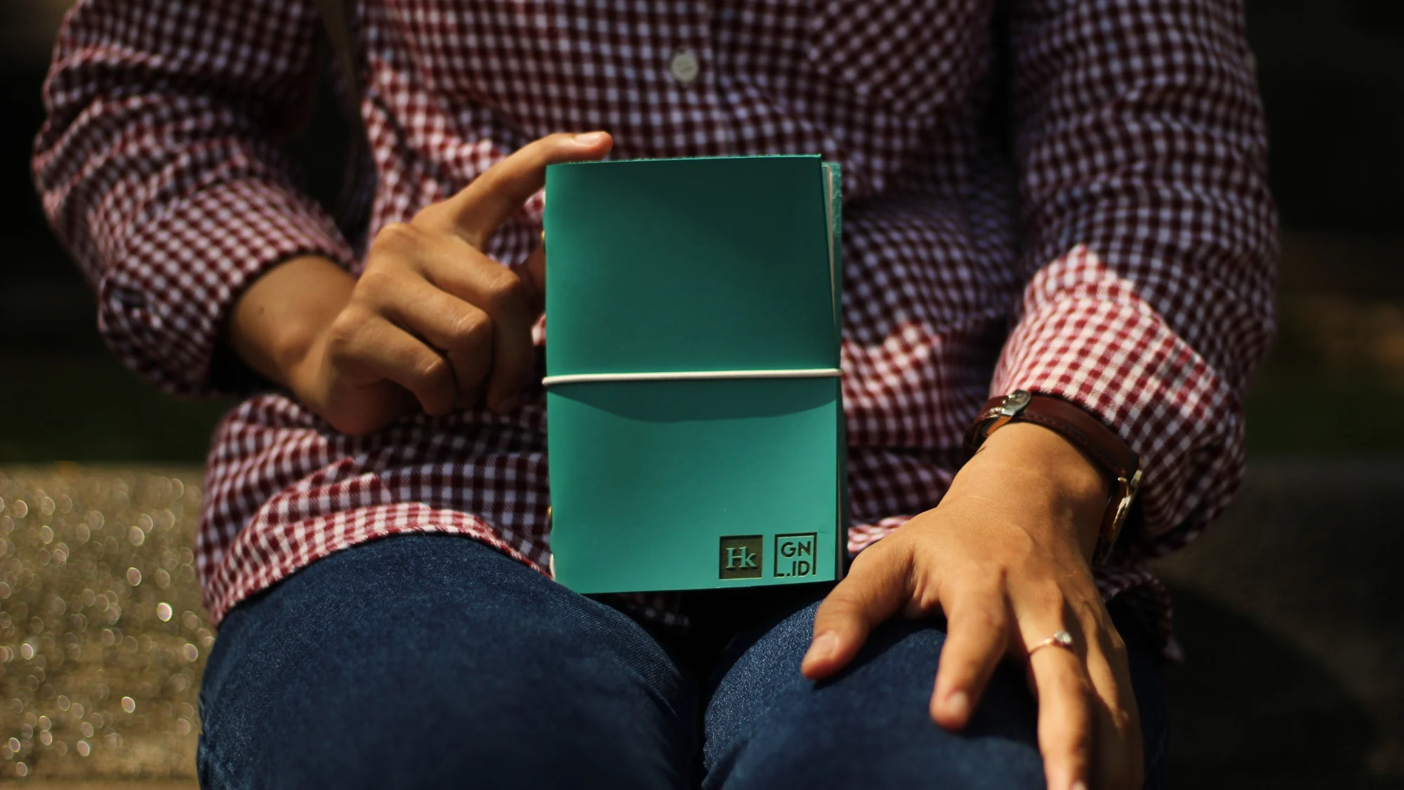 Seseorang memegang jurnal kulit warna teal dengan logo yang diemboss