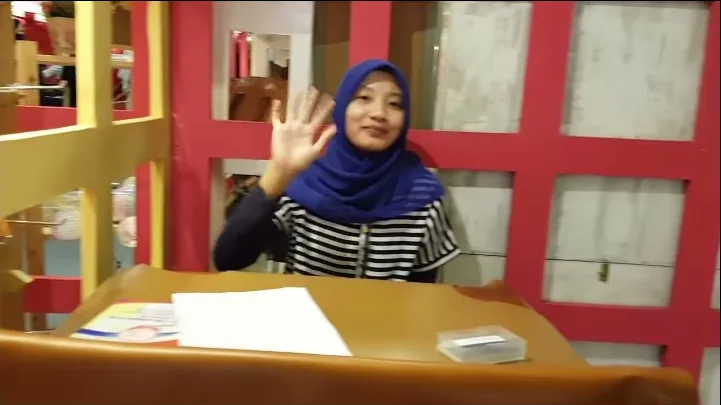 Perempuan berhijab melambai ke kamera di meja booth Hibrkraft