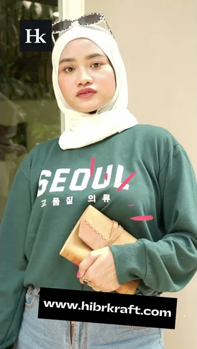 Perempuan berhijab mengenakan sweter hijau memegang jurnal kulit tan