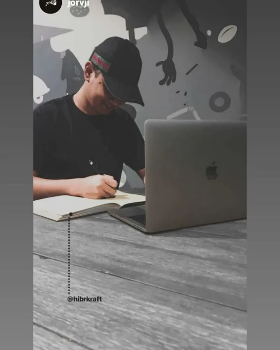 Seorang pria bertopi menulis di jurnal di samping laptop