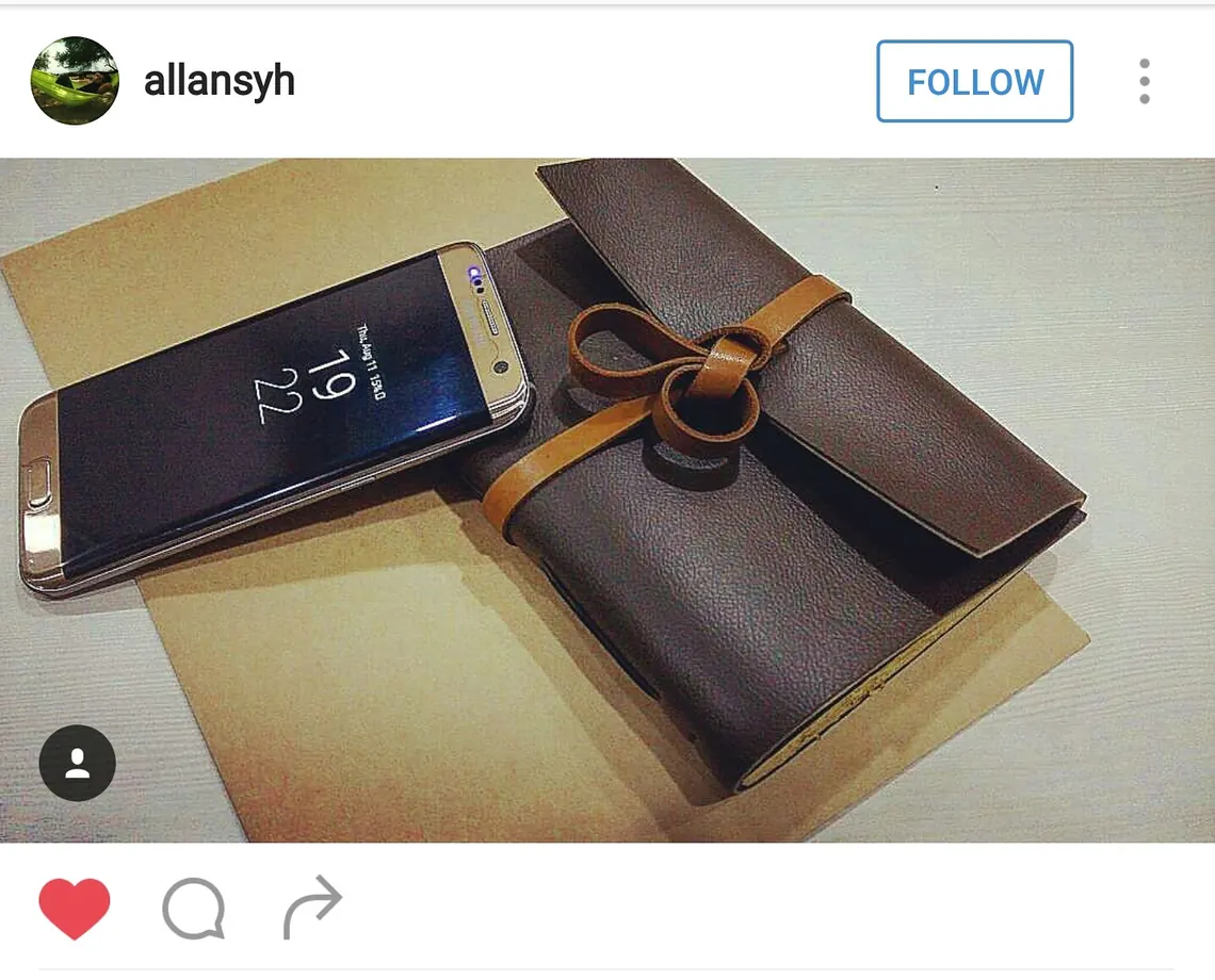 Jurnal kulit Hibrkraft di samping smartphone yang menampilkan unggahan media sosial