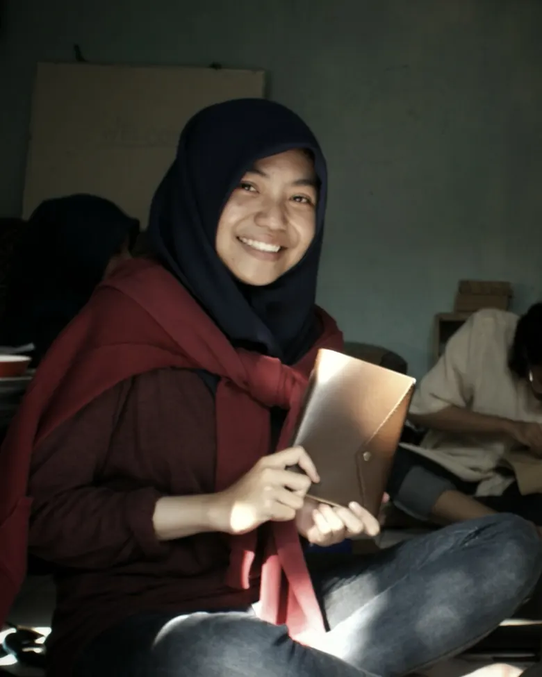 Pengrajin perempuan memegang jurnal kulit selesai di acara open house bengkel