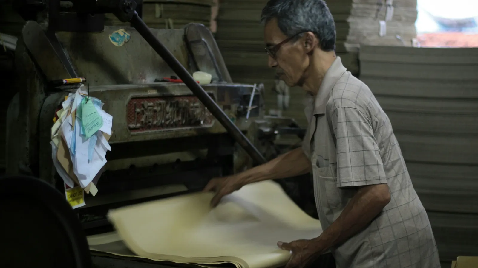 A craftsman operating an industrial paper-cutting machine for a bulk order