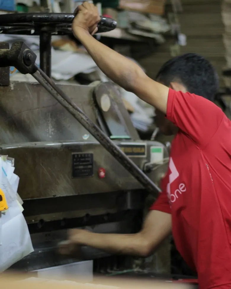 Pengrajin mengoperasikan mesin potong kertas manual di bengkel.
