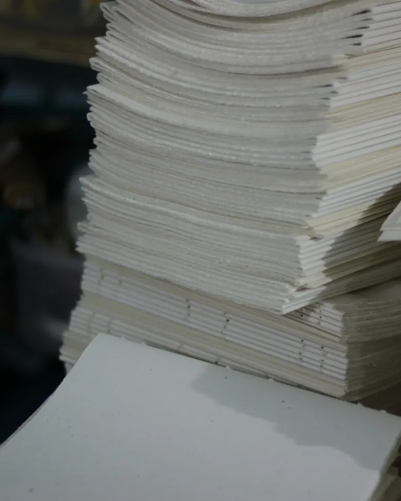 Tumpukan lipatan kertas (signature) yang telah disusun, siap dijahit.
