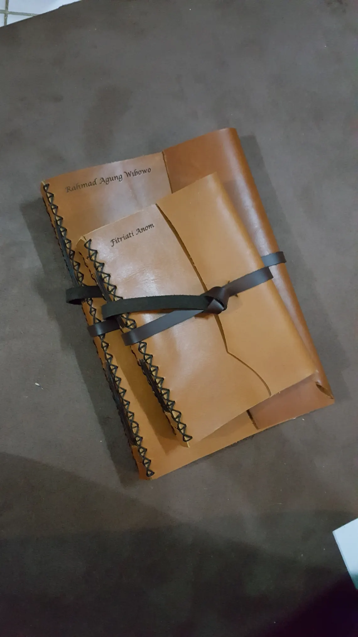 Dua jurnal kulit berdampingan, masing-masing dengan nama penerima sendiri.
