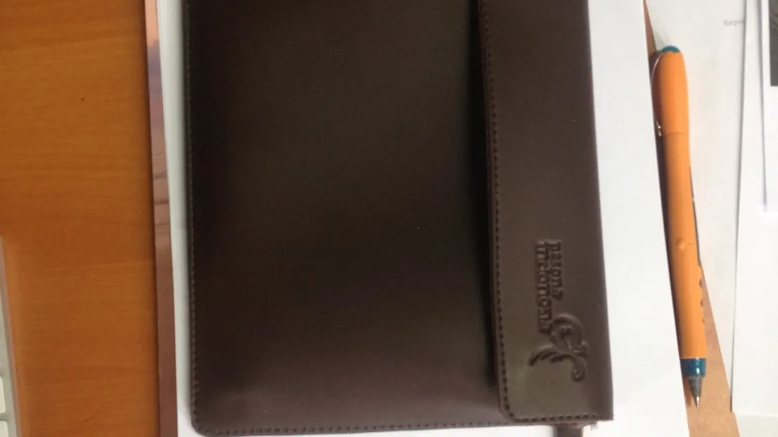 Portofolio kulit cokelat dengan logo perusahaan yang di-deboss pada sampul.