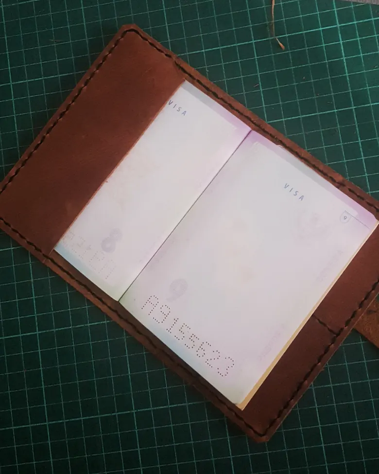 Dompet paspor kulit dengan jahitan tangan di tepinya.