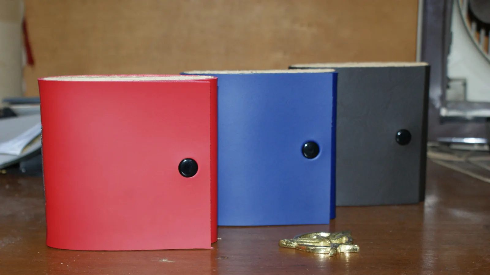 Tiga jurnal kulit berwarna merah, biru, dan hitam berjajar — contoh kombinasi model dalam satu pesanan.