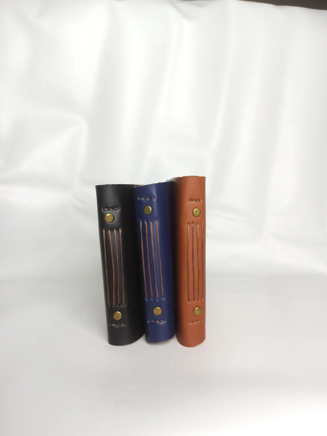 Tiga jurnal kulit dengan jahitan punggung yang terlihat, disusun berdampingan.