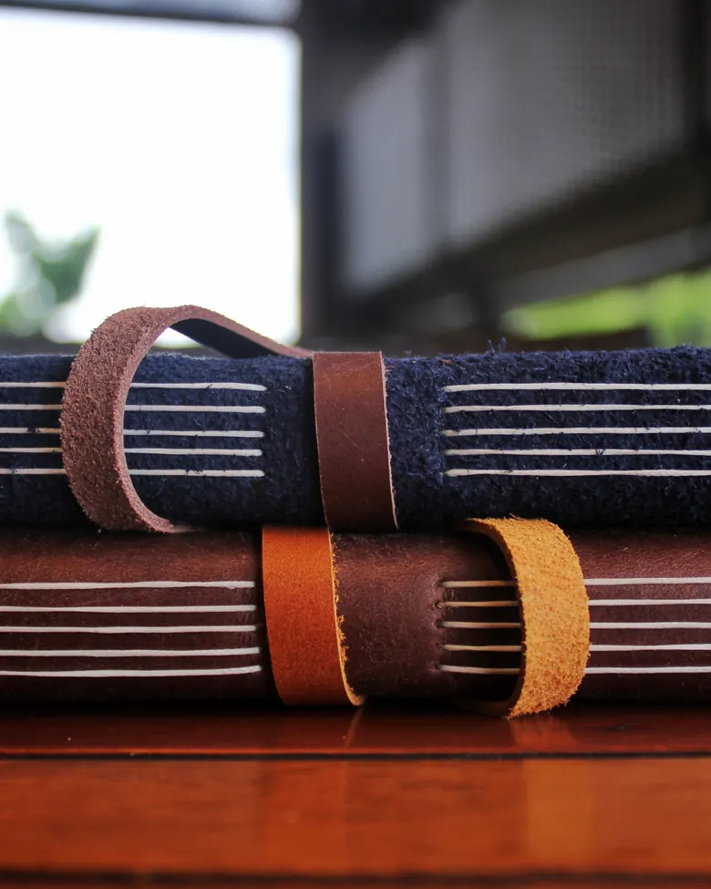 Dua jurnal kulit Hibrkraft ditumpuk dan diikat dengan tali kulit
