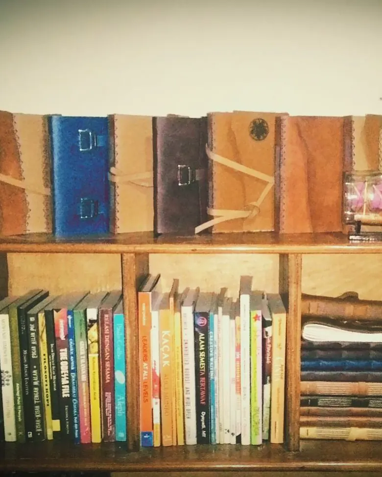 Jurnal kulit dipajang di rak buku kayu.