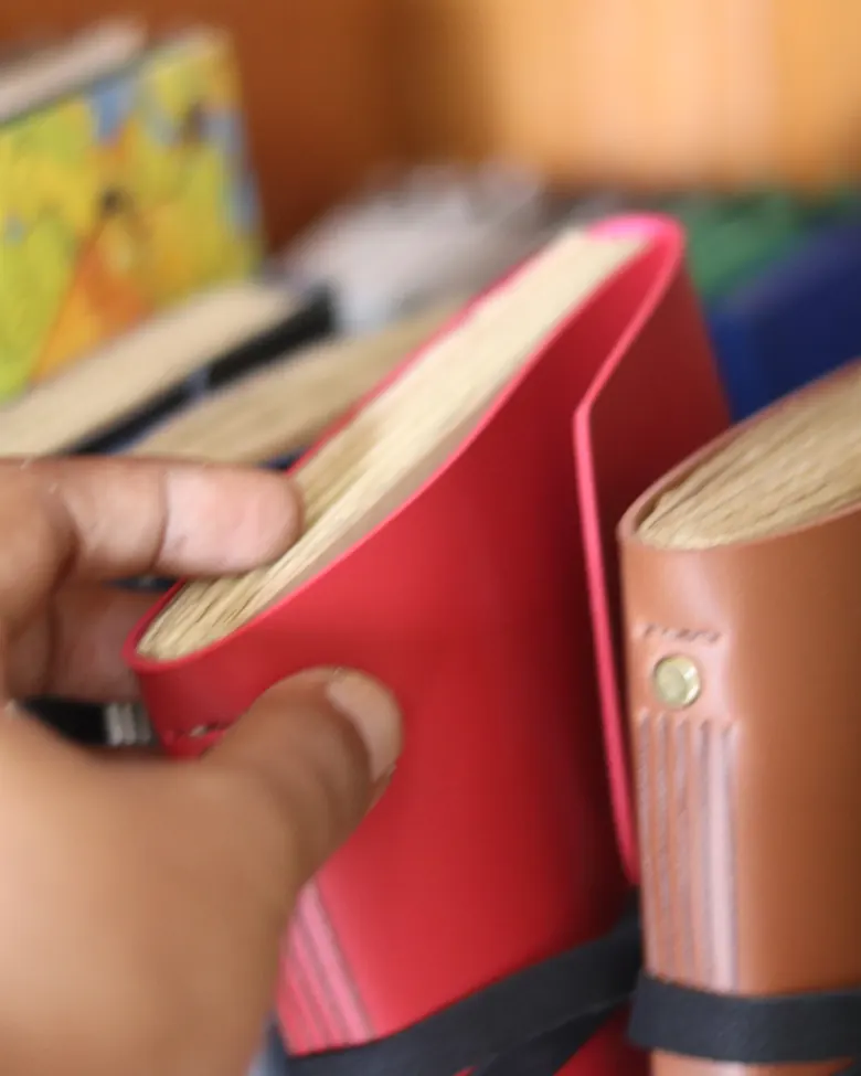 Tangan memilih satu jurnal kulit dari rak.