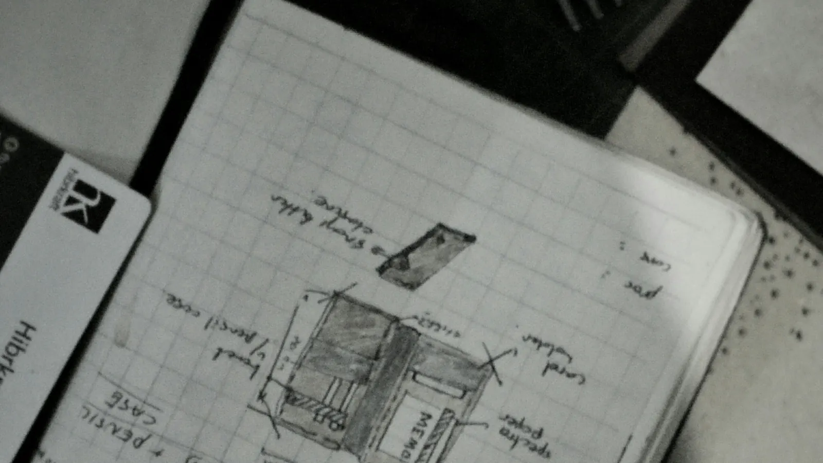 A designer's sketchbook open beside a notebook, early design work in progress.
