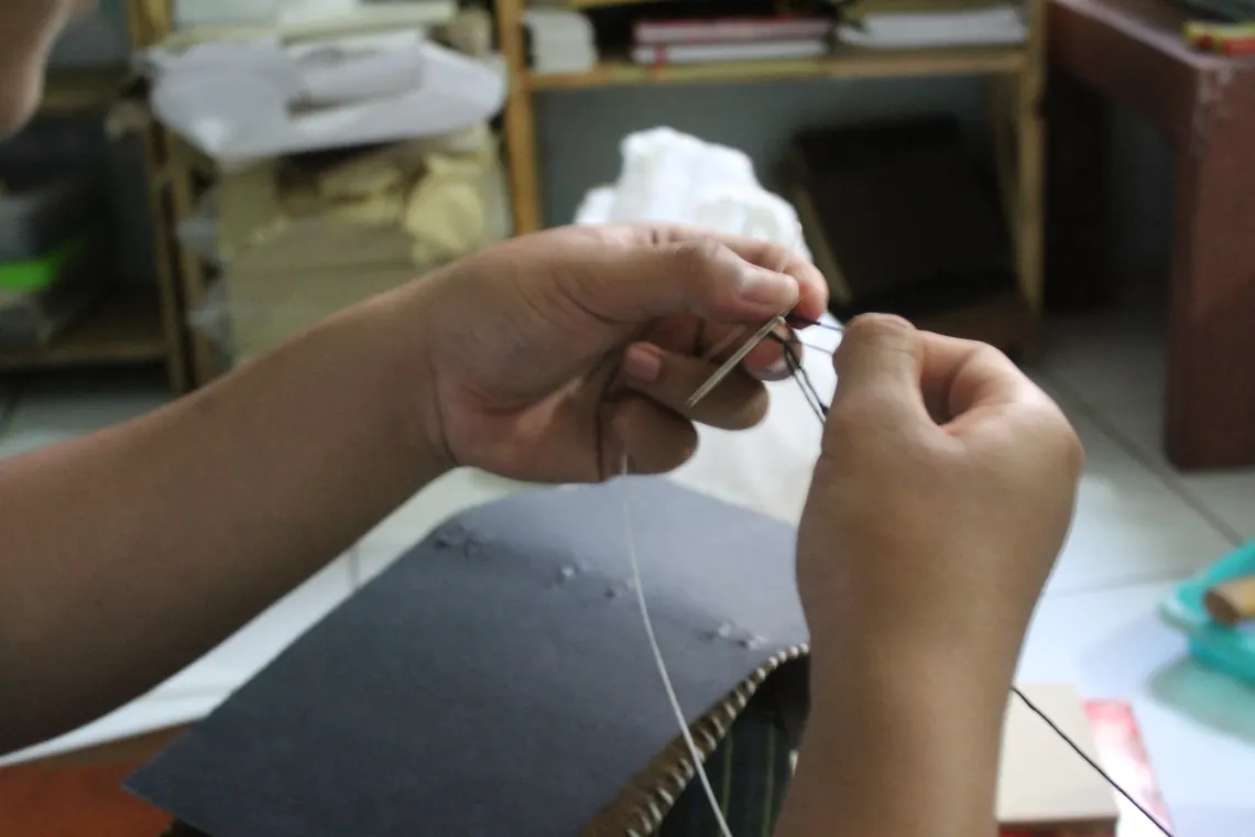 Hands stitching a leather journal cover during sample production.