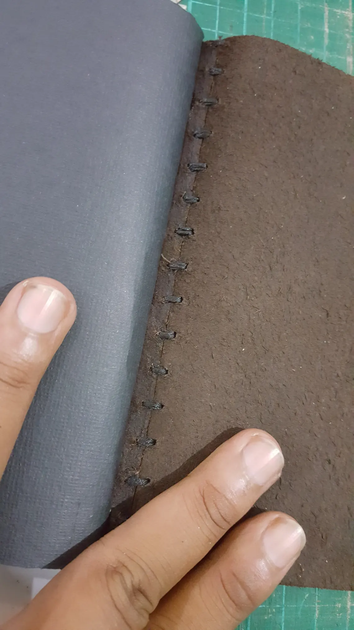 A hand stitching a leather cover to its paper block.